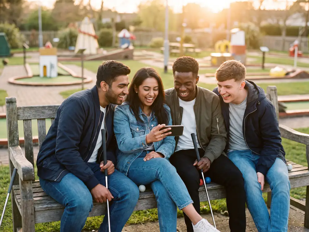 Four friends squeezed together on a bench after their round, laughing at the result on one phone